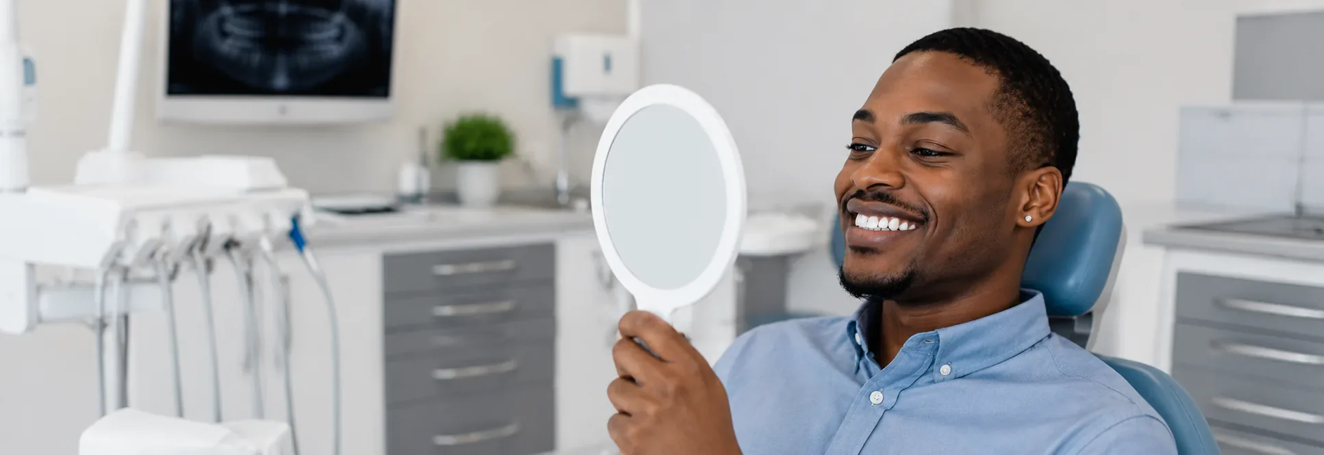 A patient in the dental chair smiling at his new restoration in a hand mirror